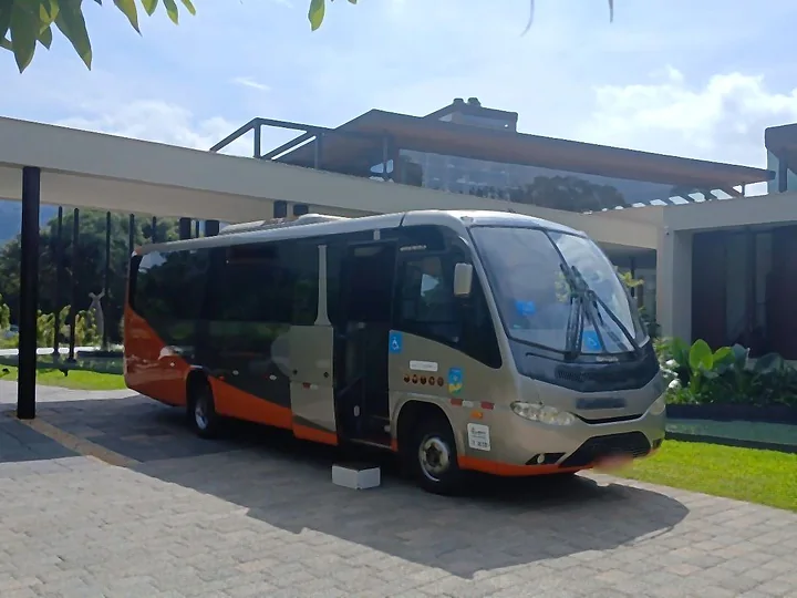 Micro-ônibus Marcopolo cinza e laranja estacionado diante de um edifício moderno com jardim