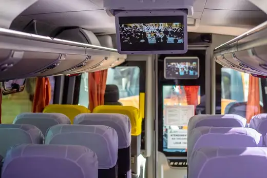 Interior de micro-ônibus com monitores de TV e cortinas