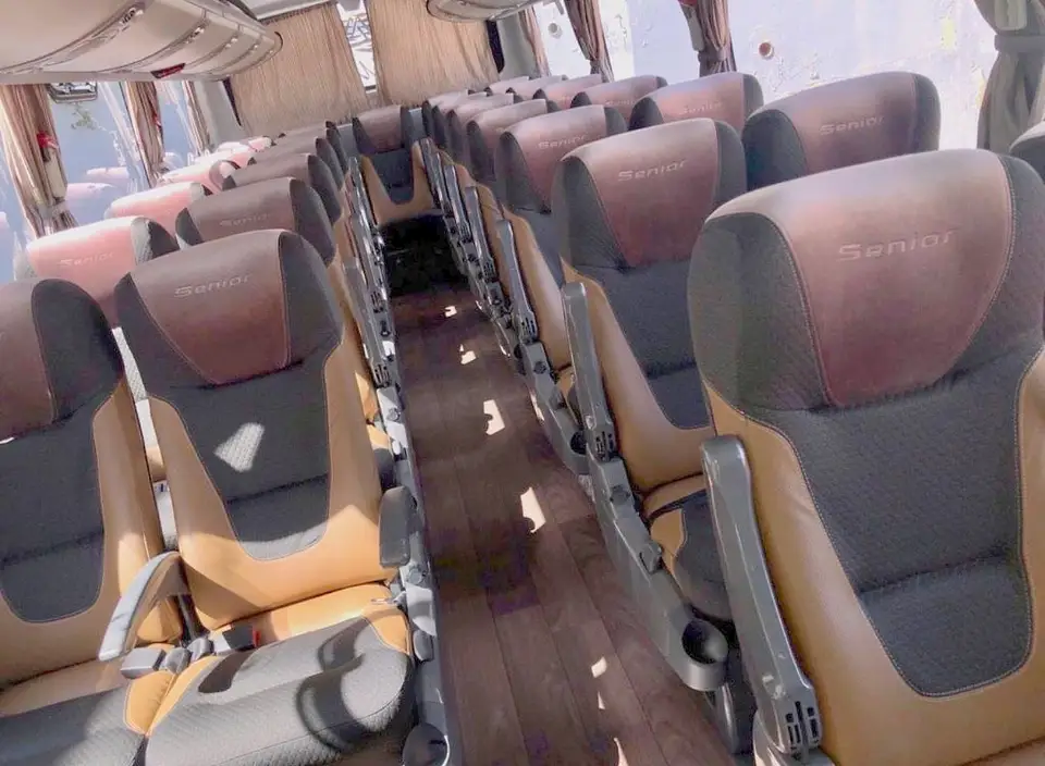 Corredor de micro-ônibus com poltronas de couro caramelo e tecido