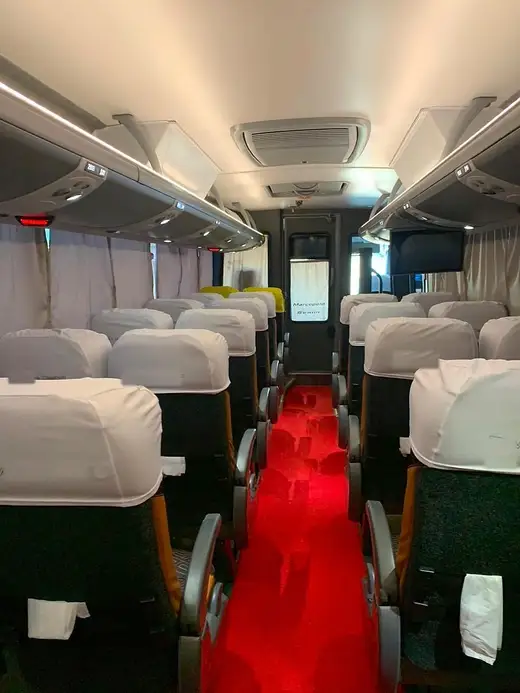 Corredor de micro-ônibus com capas brancas nas poltronas e tapete vermelho