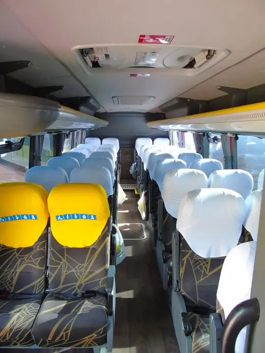 Corredor de ônibus rodoviário com poltronas estampadas e assentos preferenciais