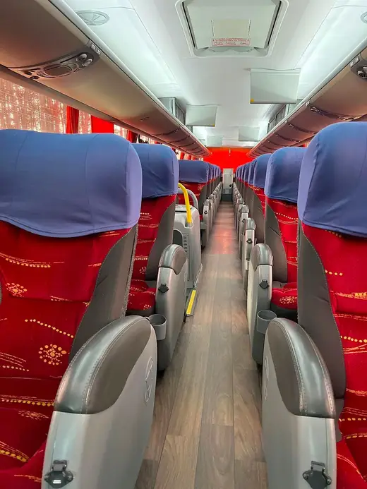 Corredor de ônibus com poltronas vermelhas e encostos azuis
