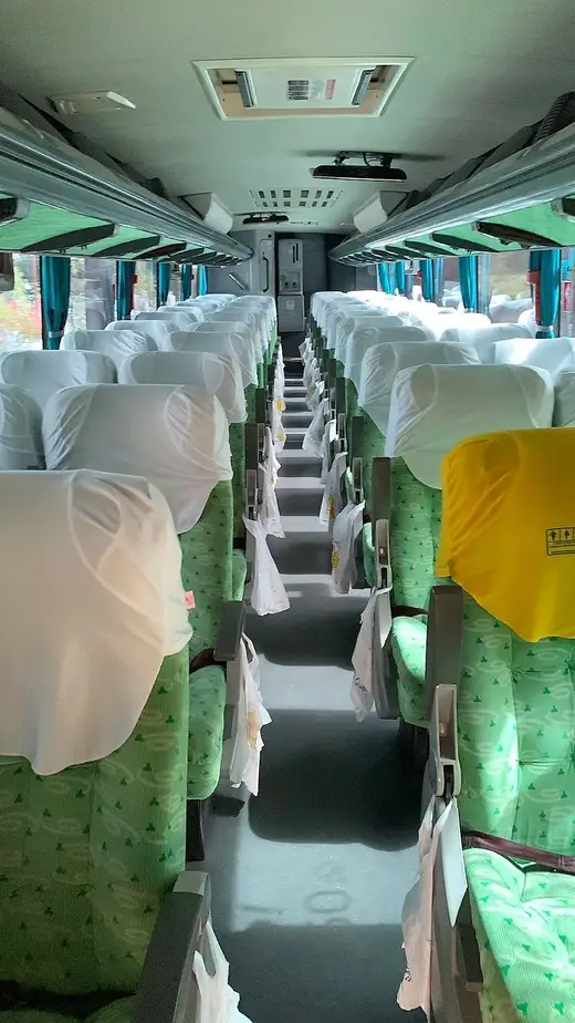 Corredor de ônibus rodoviário com poltronas cobertas por capas brancas