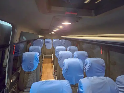 Corredor de van com poltronas de capas azuis e luzes no teto