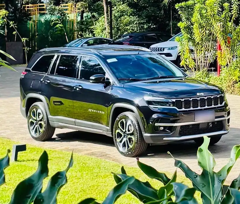 Jeep Commander preto, utilitário de 7 lugares, em pátio cercado por jardim tropical