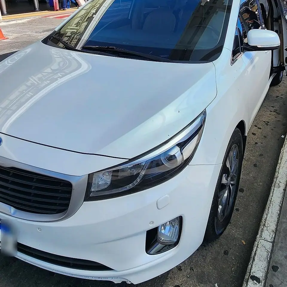 Minivan Kia Carnival branca junto ao meio-fio de embarque de um aeroporto