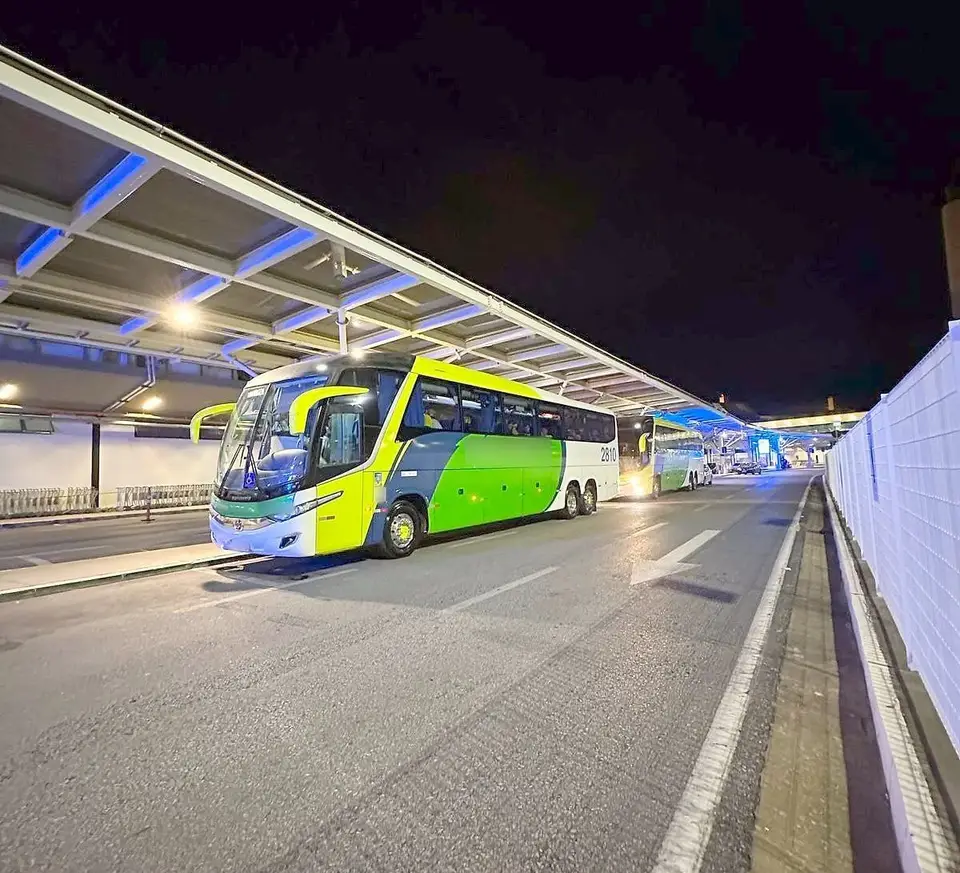 Ônibus rodoviário à noite junto à cobertura iluminada de um terminal de embarque