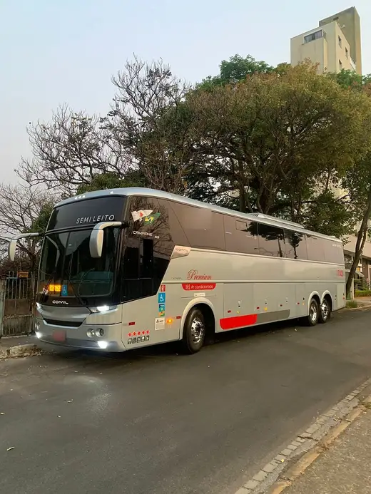Ônibus rodoviário semileito prata em rua arborizada, ao entardecer
