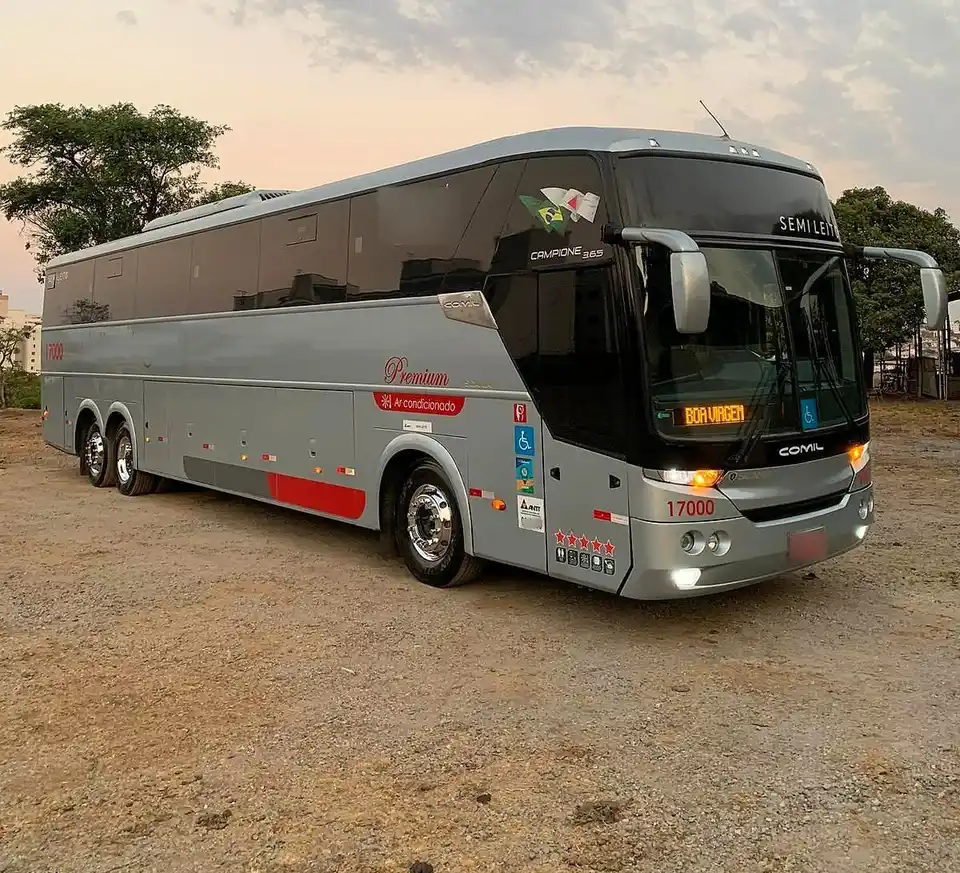 Ônibus rodoviário semileito prata estacionado em pátio de terra, ao entardecer