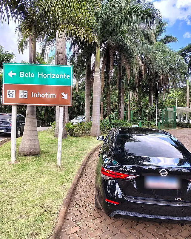 Táxi executivo preto na chegada de Inhotim, ao lado da placa que indica o caminho para o museu