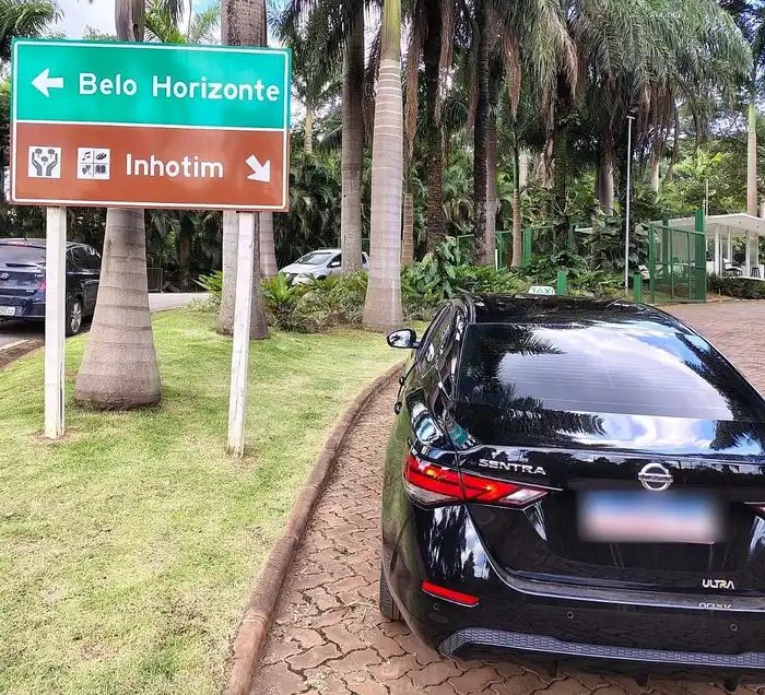 Táxi executivo preto na chegada de Inhotim, ao lado da placa que indica o caminho para o museu