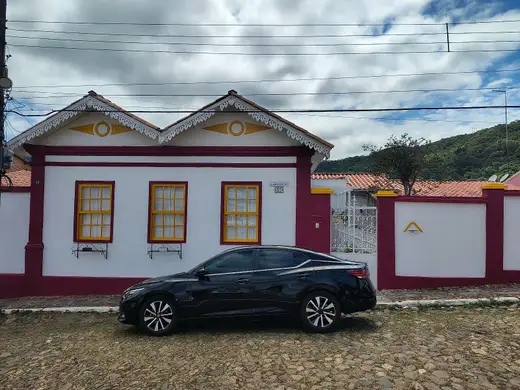 Sedan executivo preto estacionado diante de uma casa colonial com janelas amarelas
