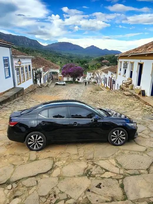 Sedan executivo preto em rua de pedra de Tiradentes, com casarios coloniais e a serra ao fundo