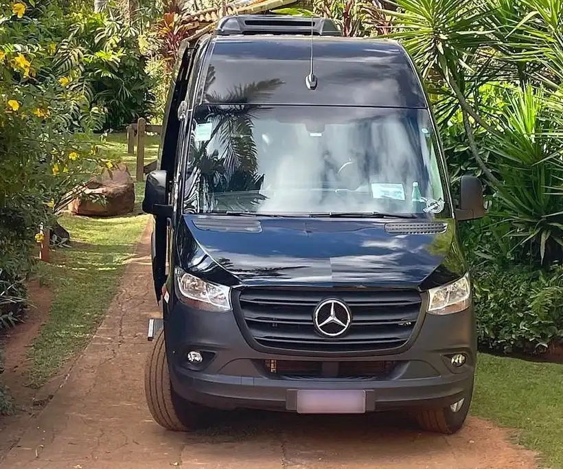 Van executiva Mercedes-Benz Sprinter preta vista de frente, entre palmeiras e jardim